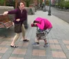 Two women appear to be engaging in playful or mock conflict on a city sidewalk with one pretending to punch while the other dodges playfully