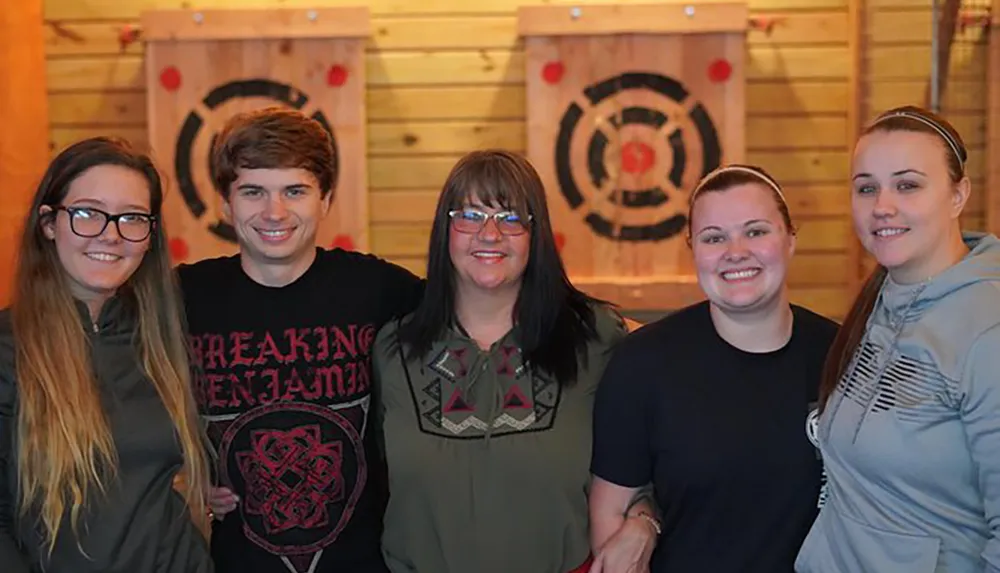 Five people are smiling for a photo in front of wooden targets used for axe throwing