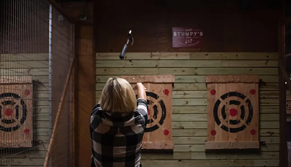 A person is seen throwing an axe towards a target in an indoor axe-throwing venue
