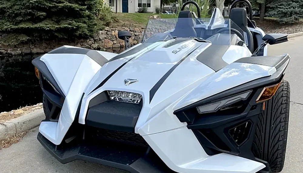 A modern white and black three-wheeled vehicle that looks like a mix between a car and a motorcycle is parked on a roadside