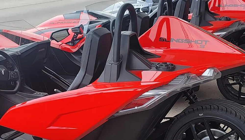 The image shows a row of red Polaris Slingshot three-wheeled vehicles featuring open cockpits and sporty designs