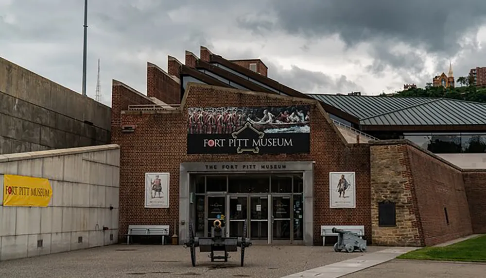 The image shows the facade of the Fort Pitt Museum with overcast skies above it