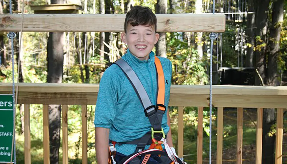 A smiling boy is wearing a safety harness likely preparing for or having just finished an outdoor ziplining or adventure course