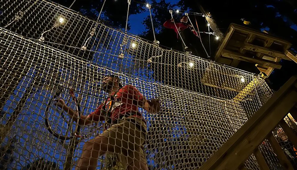 People are navigating through an outdoor high-ropes course at night illuminated by overhead lights