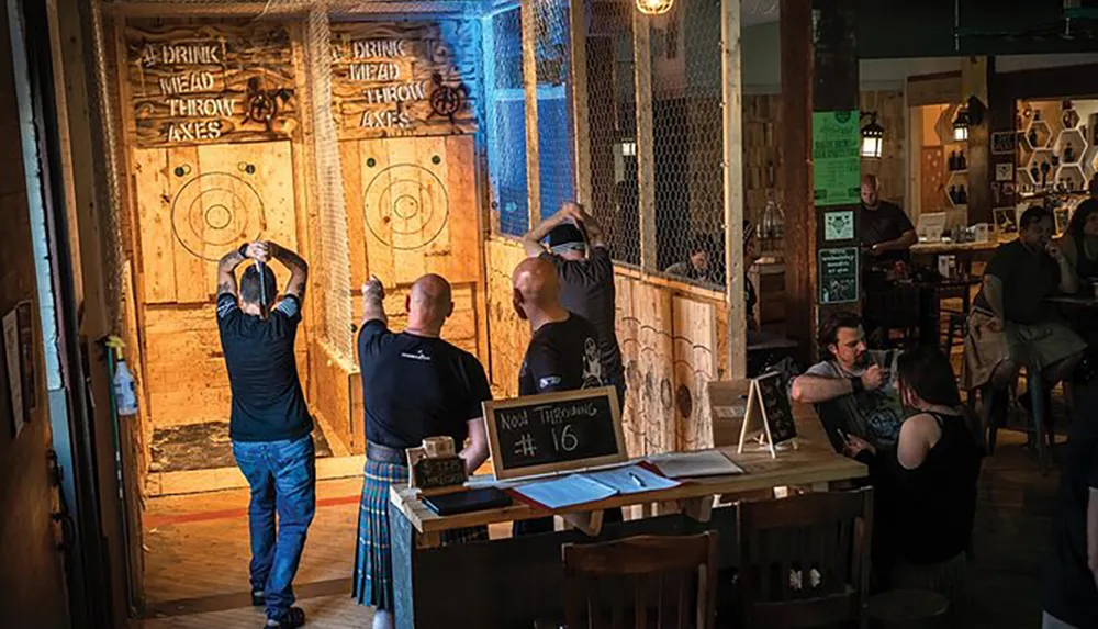 People are engaging in axe throwing at a venue that also appears to serve drinks with a casual audience in the background