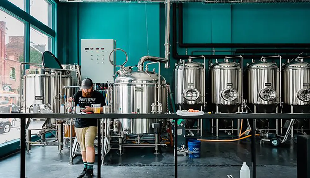 A person is working among several stainless steel brewing tanks in a modern brewery setup