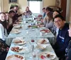 A group of people is smiling and engaging with each other around a table with the remains of a meal indicating a social gathering such as a family dinner or a festive occasion