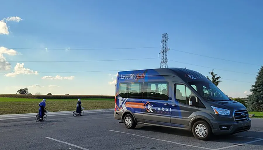 A shuttle bus branded Live life Fully is parked on the side of the road as two individuals on bicycles ride past in a rural setting.