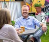 A man with a pleasant smile is enjoying a conversation and a glass of beer with a woman at an outdoor table in a colorful garden setting