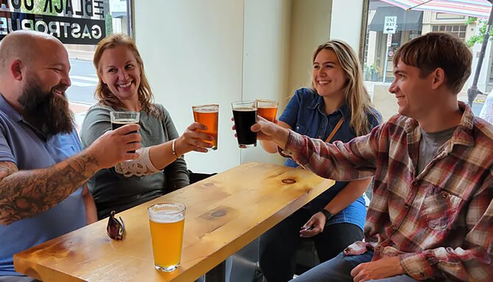 Four people are toasting with glasses of beer at a table inside a pub smiling and enjoying each others company