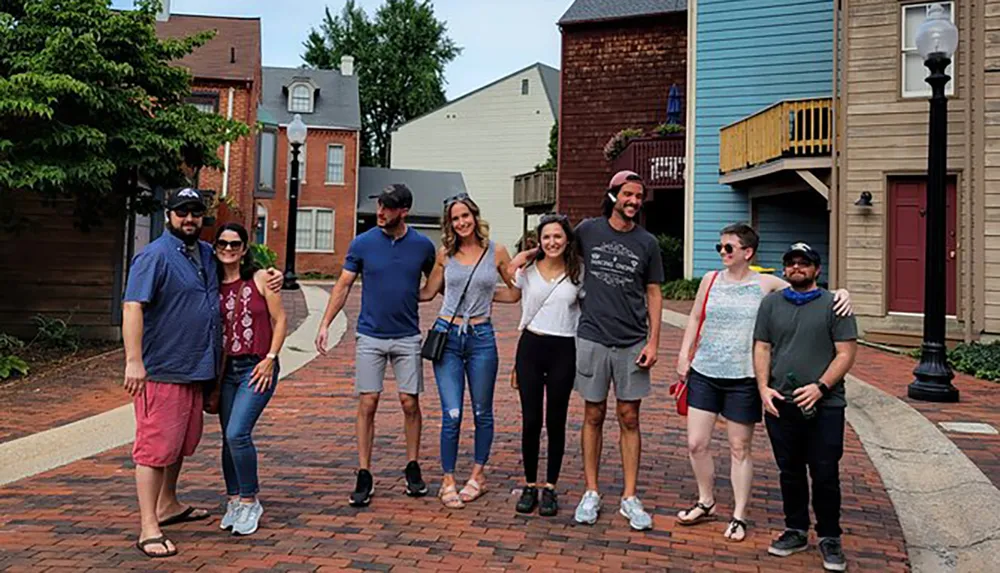 A group of seven people are smiling and posing for a photo on a brick-paved sidewalk with residential buildings in the background