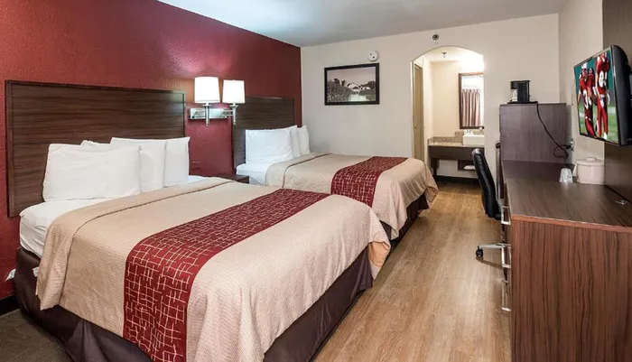 The image shows a neatly arranged hotel room with two beds a desk with a chair a mounted television and an entrance to the bathroom