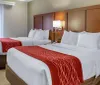The image shows a neatly made hotel room with a large bed red and white bedding a side table wall-mounted lights and an armchair creating a cozy and welcoming atmosphere