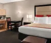 The image shows a neatly arranged modern hotel room with a large bed kitchenette dining area and contemporary furnishings
