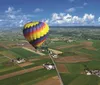 A colorful hot air balloon floats above a rural landscape with farmlands and a straight road in the early morning light