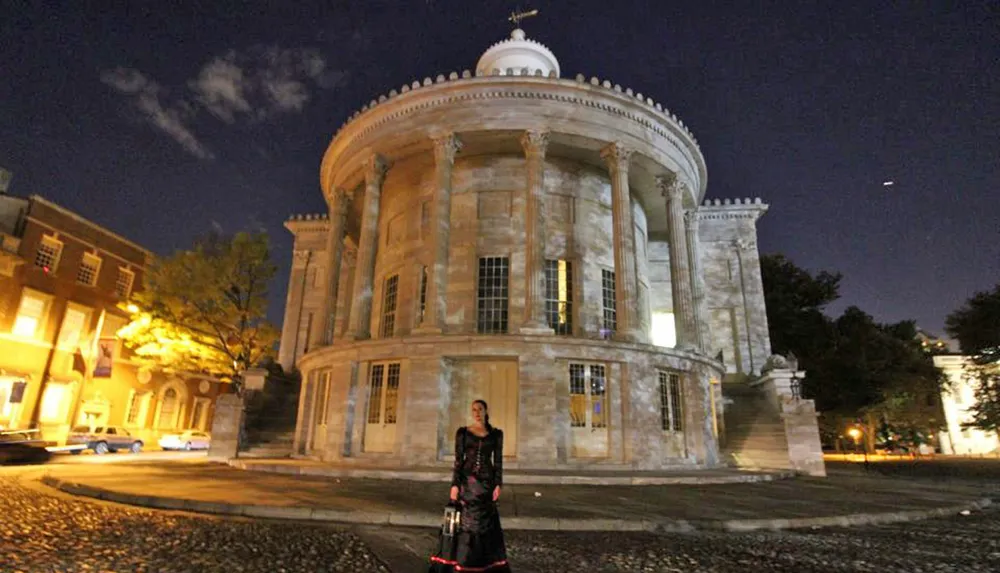 A person stands in front of a neoclassical-style building under a night sky illuminated by artificial lighting