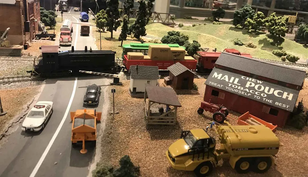 The image captures a detailed miniature model train setup featuring vehicles buildings and a landscape that simulates a small rural town