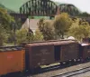 This image displays a detailed model train set featuring a Pennsylvania railroad caboose and freight cars set in a scenic miniature landscape with trees and a bridge in the background
