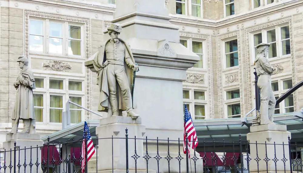 The image shows three statues of historical figures flanked by American flags in front of a classic architectural building with detailed facades