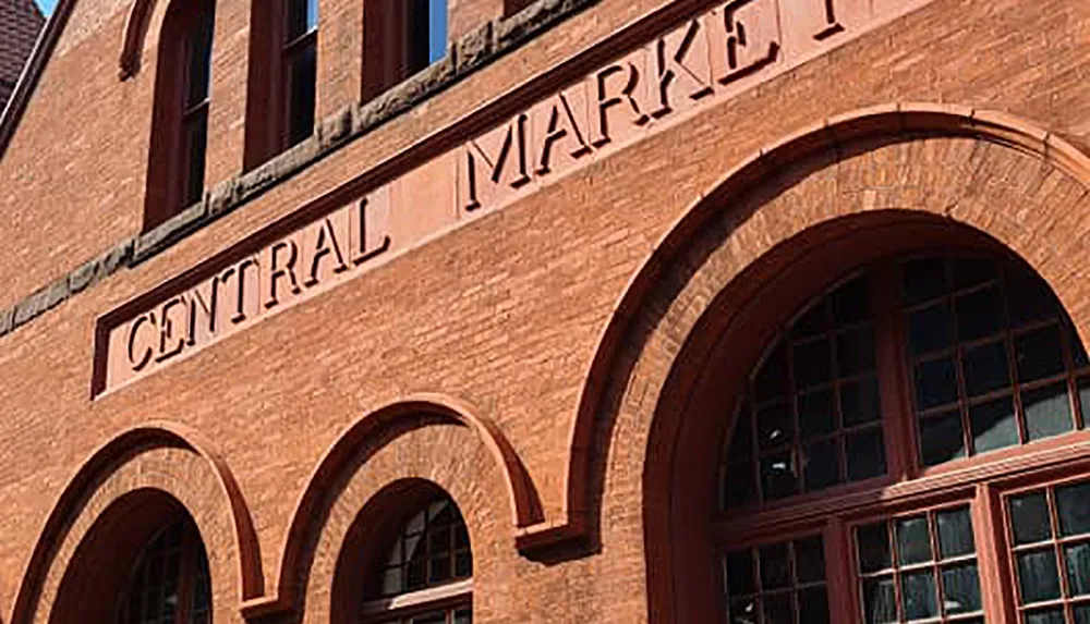 The image shows a close-up view of a brick building with the words CENTRAL MARKET in raised lettering arching over large windows