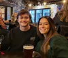 A smiling man and woman are sitting at a table with pints of beer in a cozy pub setting