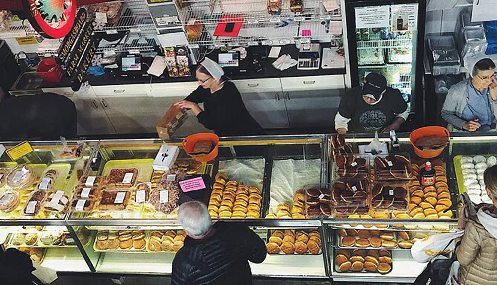 Workers are attending to customers at a bustling bakery counter filled with an assortment of bread and pastries