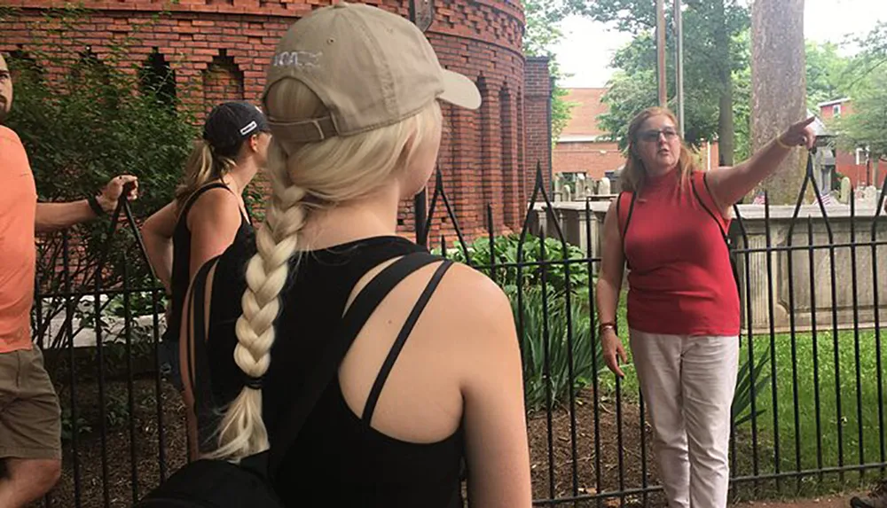 A group of people is listening to a woman who appears to be giving a tour or presentation outdoors