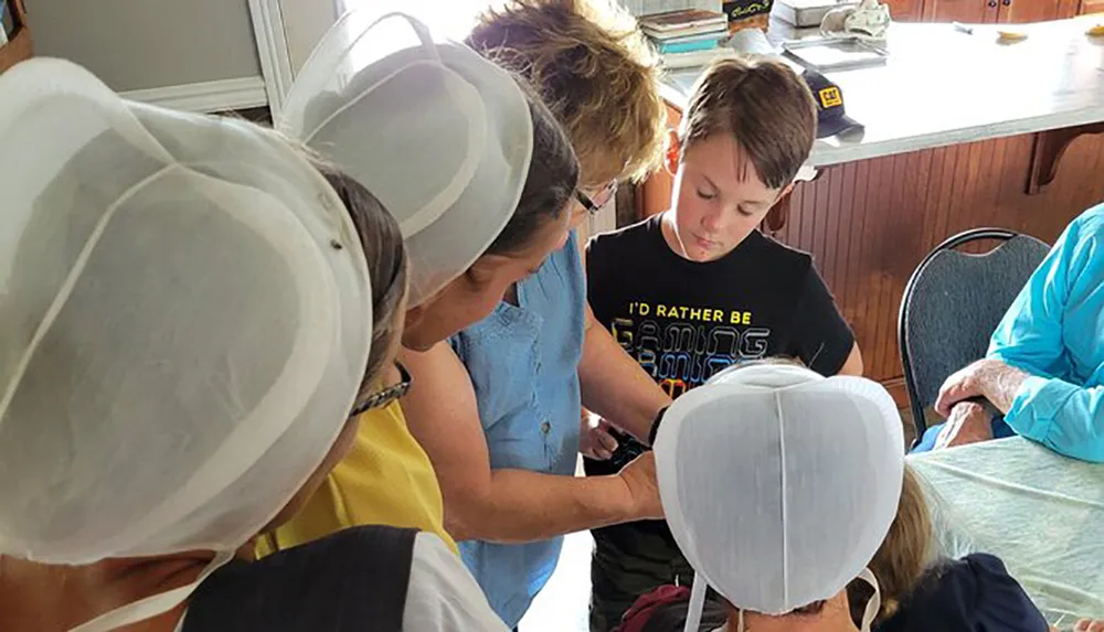 A group of people including children wearing beekeeper hats focus on an activity at a table