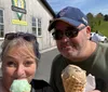 Two people are taking a selfie outside a creamery each holding an ice cream cone and smiling on a sunny day