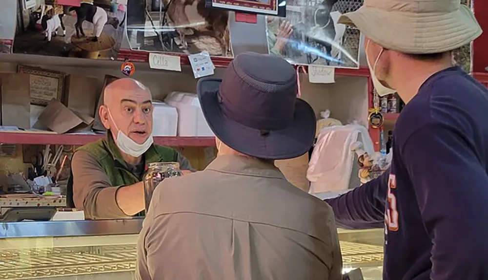 An employee at a food counter appears surprised or animated during an interaction with two customers wearing hats