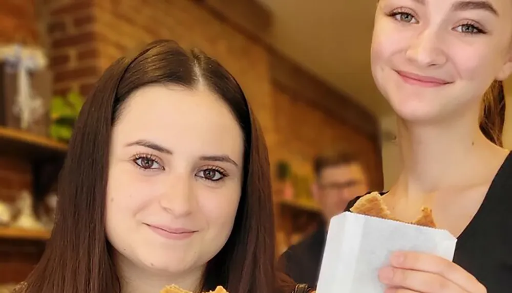 Two young women are smiling at the camera one holding what appears to be a sandwich
