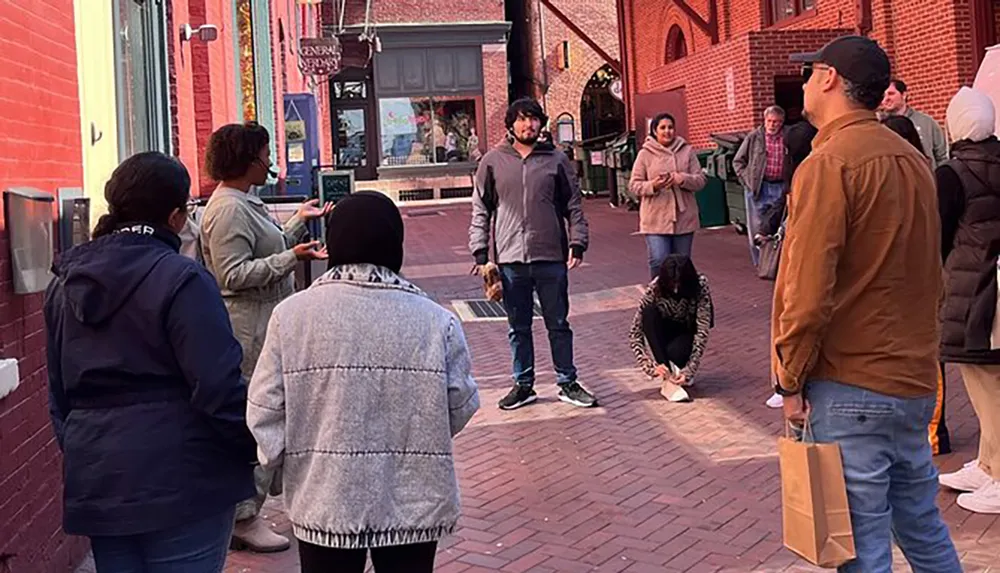 A group of people is gathered on a brick-paved street possibly listening to a speaker or waiting for an event