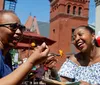 Two women are laughing joyfully while sharing a meal outdoors on a sunny day