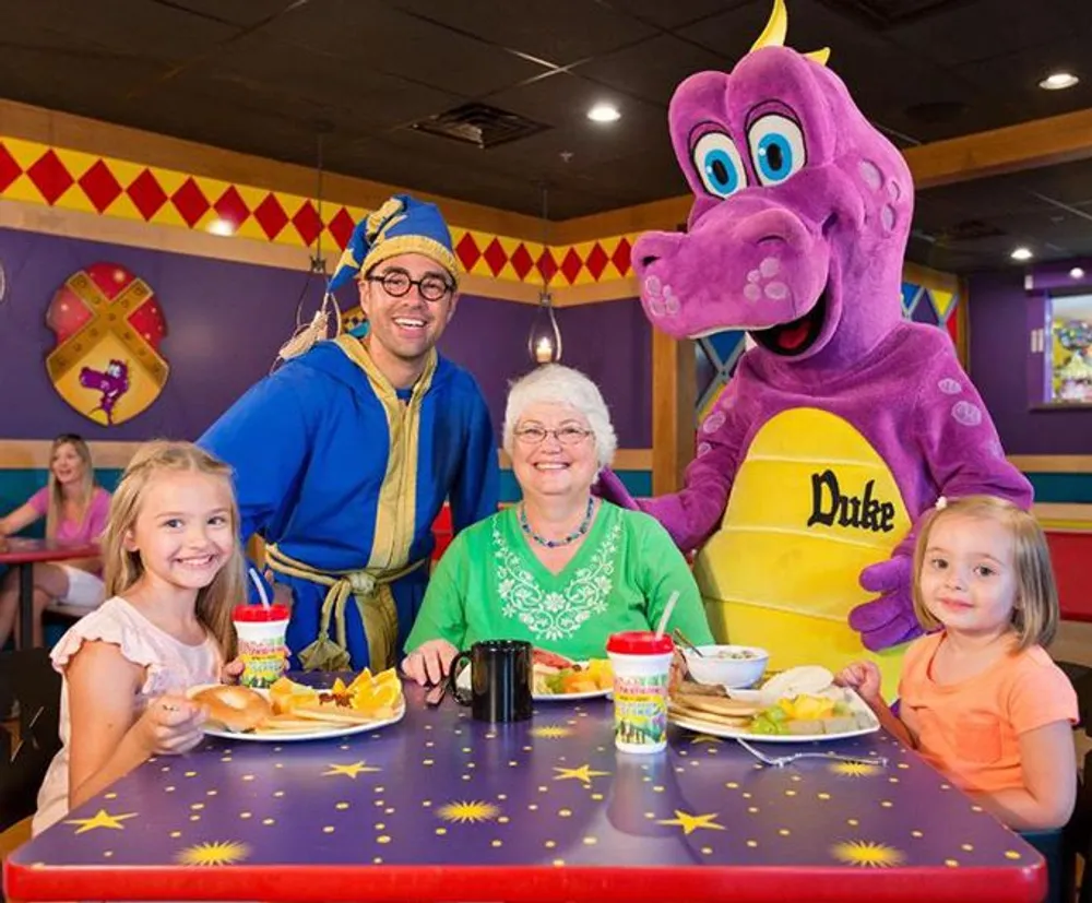 A family is posing with a person in a purple dragon costume and a performer dressed as a genie at a colorful themed restaurant