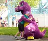 Children are joyfully riding on a colorful frog-themed amusement park ride on a sunny day