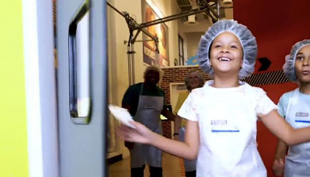 Children wearing hairnets and aprons are smiling happily likely engaged in a fun educational activity related to food preparation or hygiene