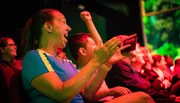 An audience member is expressing excitement and joy with a wide smile and clenched fist at an event.