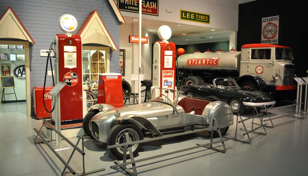 The image shows a vintage automotive-themed exhibit featuring classic cars an antique gas pump a tire advertisement and a retro oil tank truck