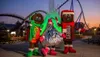 Three people in festive candy-themed costumes stand in front of a roller coaster at dusk.