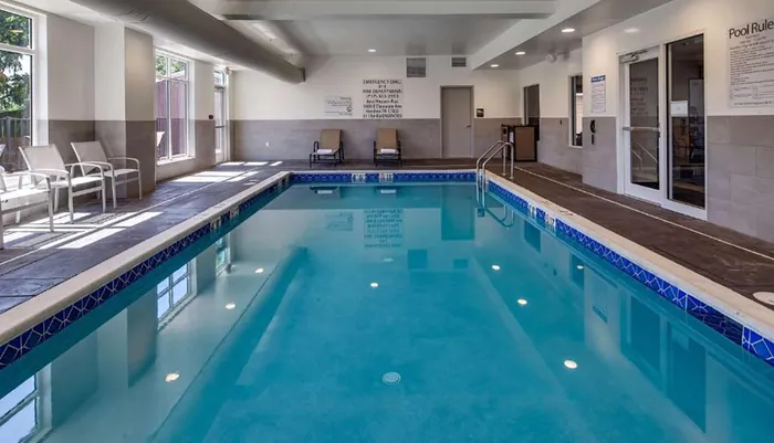 An indoor swimming pool with clear blue water surrounded by lounge chairs and safety guidelines displayed on the wall