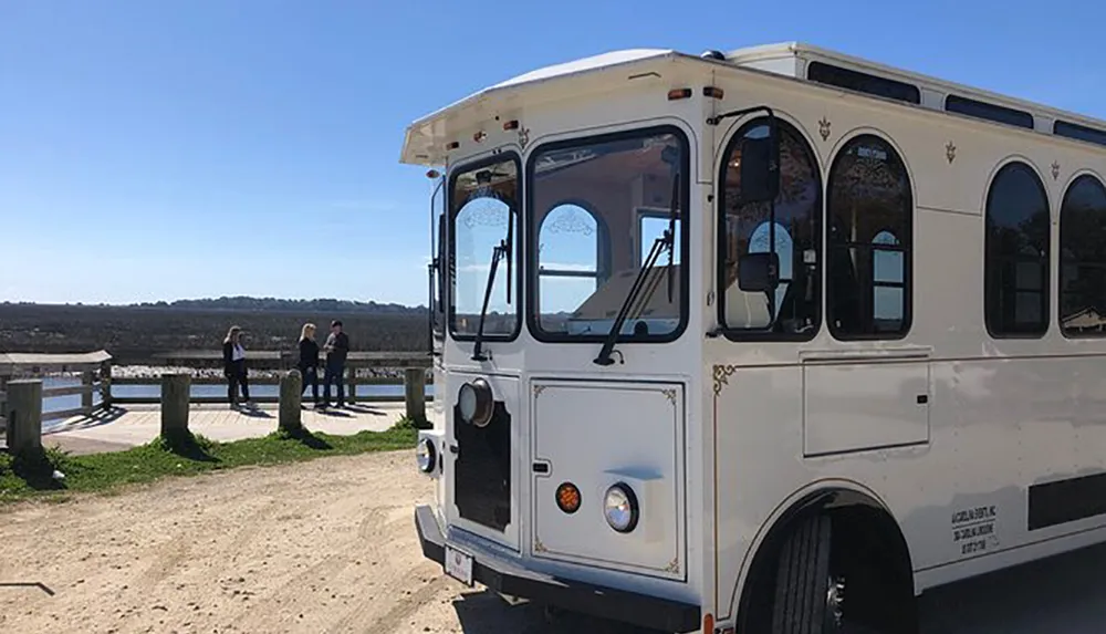 A vintage-style white trolley bus is parked beside a scenic overlook where two people stand chatting