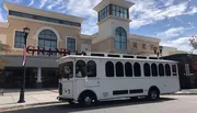 A trolley-style bus is parked in front of a building with a sign that reads 