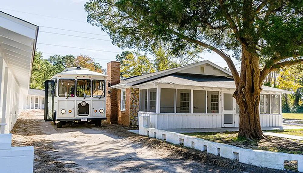 A white trolley bus is parked beside a traditional single-story house with a screened porch under a clear sky