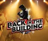 This image is a promotional graphic featuring silhouettes and images of a male and a female performer with spotlights and the title BACK IN THE BUILDING in bold lettering suggesting a musical or entertainment event