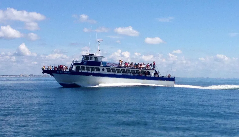 A passenger boat is cruising on the sea under a blue sky dotted with clouds carrying several people on its decks