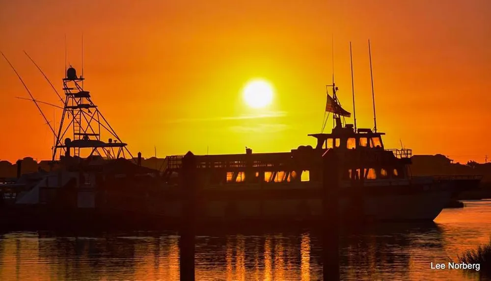 The image shows a serene sunset backdrop over a harbor where silhouettes of boats are moored casting reflections on the water