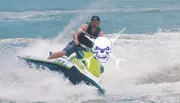 A person is riding a jet ski on choppy water with a stylized skull and crossbones graphic superimposed on the image.