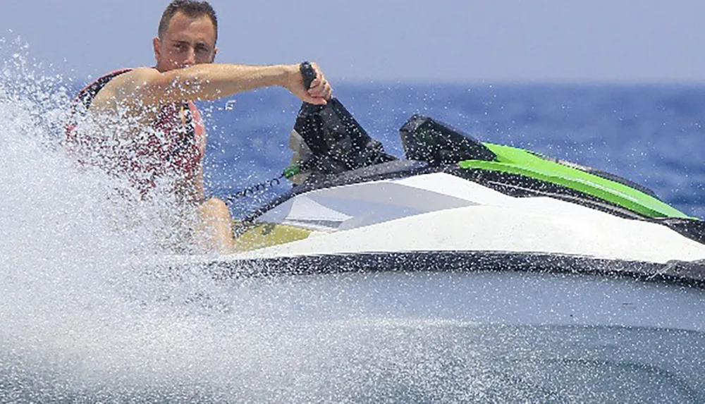 A person is actively riding a jet ski making a sharp turn with water spraying around