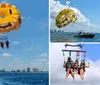 Two people are parasailing under a smiling face-decorated parachute against a clear blue sky