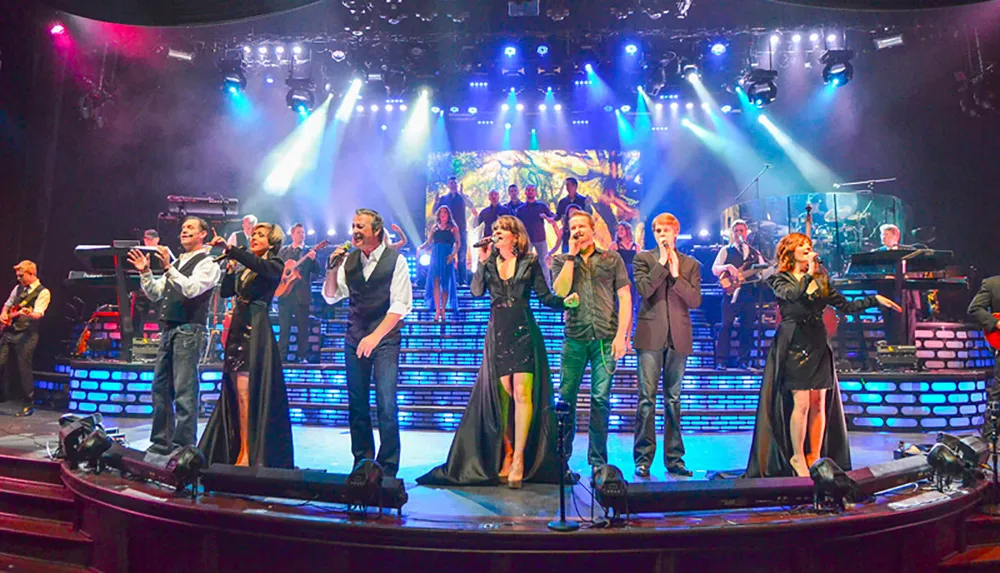 A group of performers is singing onstage with a live band and colorful stage lighting in the background